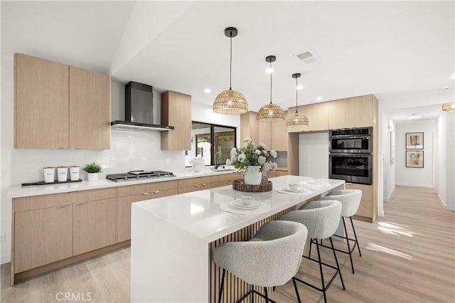 4700 Emerald Ave, La Verne, CA 91750 - kitchen with wall chimney exhaust hood, appliances with stainless steel finishes, light brown cabinets, light wood-style floors, and a kitchen breakfast bar