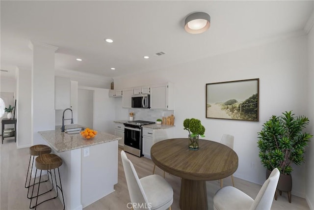 11490 Autumn St, Adelanto, CA 92301 - kitchen featuring appliances with stainless steel finishes, white cabinets, a kitchen bar, light stone countertops, and light wood finished floors