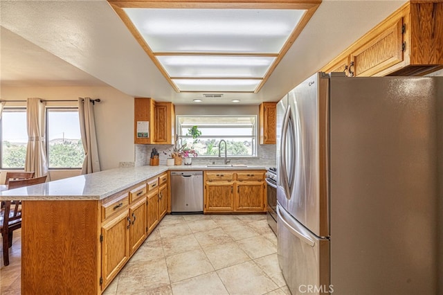 14320 Kiptree Dr, Lake Hughes, CA 93532 - kitchen featuring appliances with stainless steel finishes, a peninsula, tasteful backsplash, brown cabinets, and light tile patterned floors