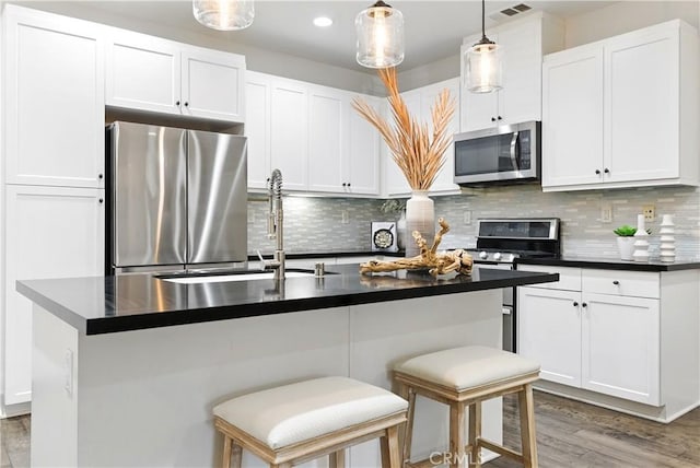 28 Sembrio St, Rancho Mission Viejo, CA 92694 - kitchen featuring appliances with stainless steel finishes, dark countertops, light wood-style floors, white cabinets, and decorative light fixtures