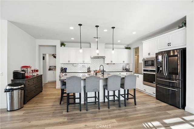 11715 Periwinkle Pl, Jurupa Valley, CA 91752 - kitchen with appliances with stainless steel finishes, recessed lighting, tasteful backsplash, a breakfast bar area, and light wood-style flooring