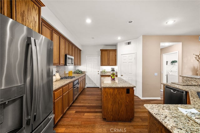 13014 Bermuda Ave, Chino, CA 91710 - kitchen with stainless steel appliances, dark wood-style floors, brown cabinets, a center island, and light stone counters