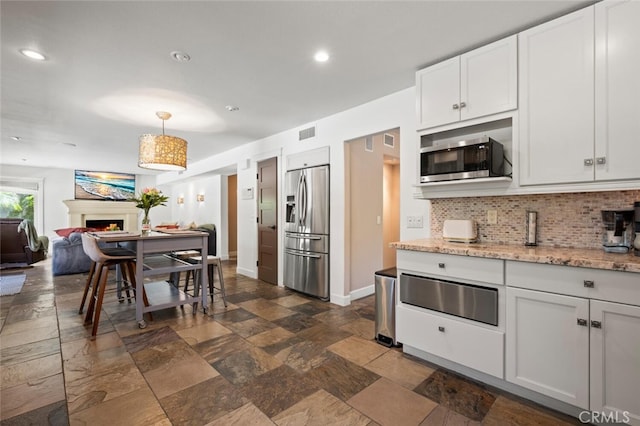 27681 Paseo Esteban, San Juan Capistrano, CA 92675 - kitchen featuring stainless steel appliances, a warming drawer, stone tile flooring, tasteful backsplash, and a warm lit fireplace