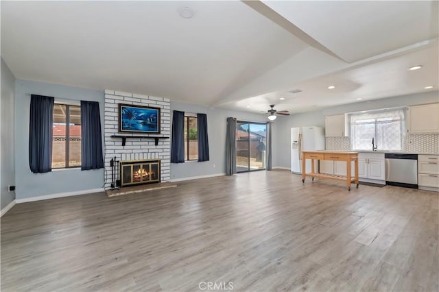 2294 Daisy Way, Hemet, CA 92545 - unfurnished living room featuring light wood-type flooring, a brick fireplace, a ceiling fan, plenty of natural light, and lofted ceiling