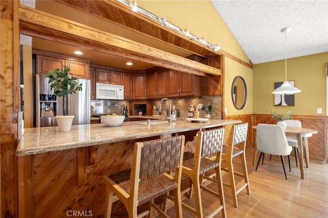 26017 Redbluff Dr, Calabasas, CA 91302 - kitchen with white microwave, stainless steel fridge, a wainscoted wall, a peninsula, and brown cabinetry