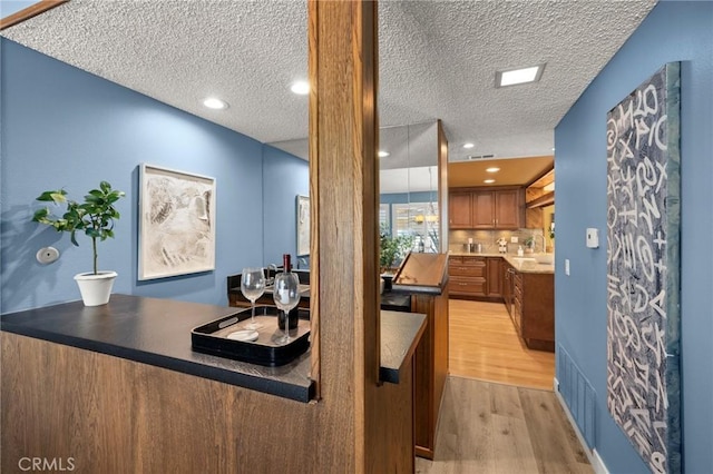 26017 Redbluff Dr, Calabasas, CA 91302 - kitchen with light wood finished floors, brown cabinetry, a textured ceiling, and tasteful backsplash