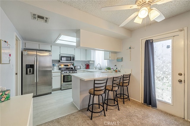 43840 Bobby Jones Dr Unit 22, Lancaster, CA 93536 - kitchen with appliances with stainless steel finishes, a peninsula, light countertops, a breakfast bar, and a textured ceiling