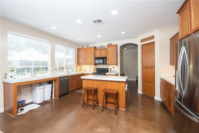 8718 Snowmass Peak Way, Riverside, CA 92508 - kitchen with stainless steel appliances, arched walkways, a kitchen island, finished concrete flooring, and brown cabinets