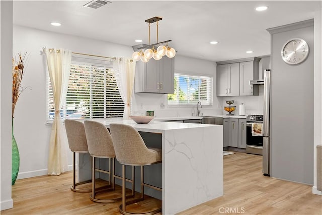 6002 Calvin Cir, Huntington Beach, CA 92647 - kitchen with gray cabinetry, stainless steel stove, a peninsula, a kitchen bar, and light wood-style flooring
