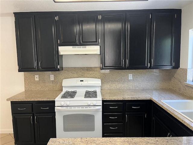 7711 Cartilla Ave, Fontana, CA 92336 - kitchen featuring white gas range, under cabinet range hood, dark cabinetry, and light countertops