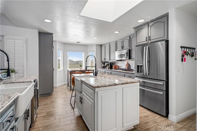 32175 Cedarcroft Rd, Acton, CA 93510 - kitchen featuring stainless steel appliances, light wood-type flooring, tasteful backsplash, gray cabinetry, and a kitchen island with sink