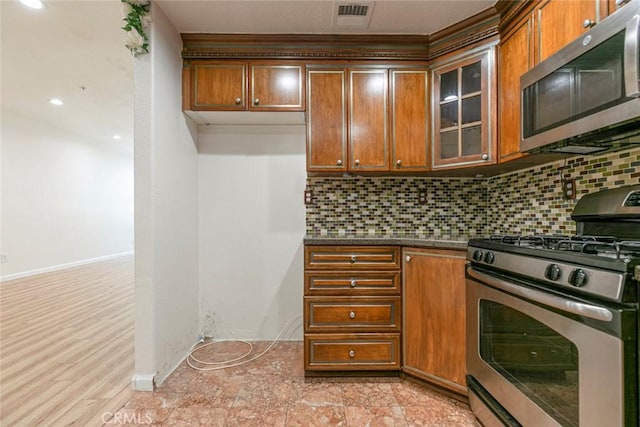 16940 Chatsworth St Unit 208, Granada Hills, CA 91344 - kitchen featuring appliances with stainless steel finishes, dark countertops, tasteful backsplash, brown cabinetry, and glass insert cabinets