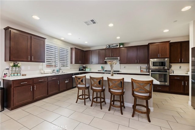 9574 Alta Cresta Ave, Riverside, CA 92508 - kitchen with stainless steel appliances, light countertops, under cabinet range hood, a kitchen bar, and a center island with sink