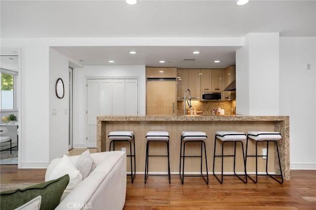 447 N Doheny Dr Unit 104, Beverly Hills, CA 90210 - kitchen with stainless steel microwave, a breakfast bar area, light wood-style flooring, a peninsula, and backsplash