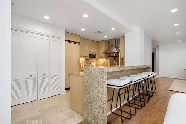 447 N Doheny Dr Unit 104, Beverly Hills, CA 90210 - kitchen featuring wall chimney range hood, stainless steel microwave, decorative backsplash, recessed lighting, and light stone countertops