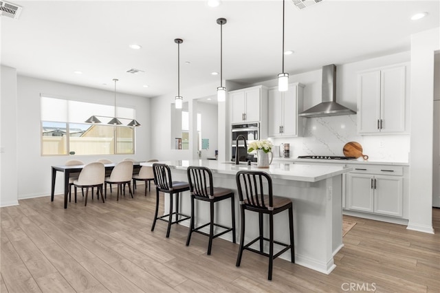 32886 Birchall Ct, Winchester, CA 92596 - kitchen with wall chimney range hood, a center island with sink, light wood-style floors, light countertops, and recessed lighting