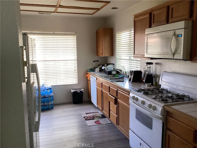 13489 Buggy Whip Ct, Victorville, CA 92392 - kitchen featuring white appliances, tile counters, light wood-style flooring, and brown cabinets