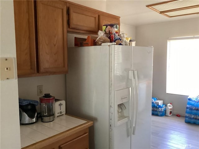 13489 Buggy Whip Ct, Victorville, CA 92392 - kitchen with white refrigerator with ice dispenser, tile counters, wood finished floors, and brown cabinetry