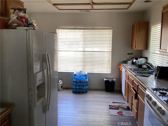 13489 Buggy Whip Ct, Victorville, CA 92392 - kitchen featuring white appliances, tile counters, light wood finished floors, and brown cabinetry