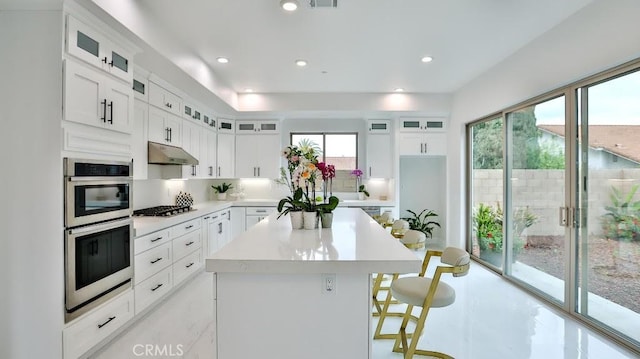 17413 Siena Ln, Fountain Valley, CA 92708 - kitchen with stainless steel appliances, under cabinet range hood, a kitchen island, a kitchen breakfast bar, and light countertops