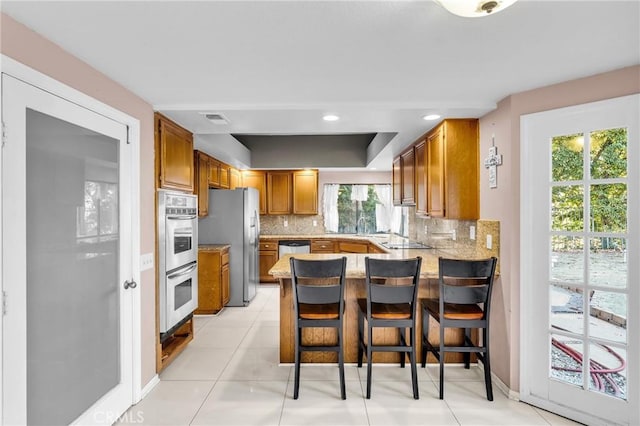 1549 Hillcrest Dr, Pomona, CA 91768 - kitchen featuring appliances with stainless steel finishes, a peninsula, tasteful backsplash, brown cabinetry, and a raised ceiling