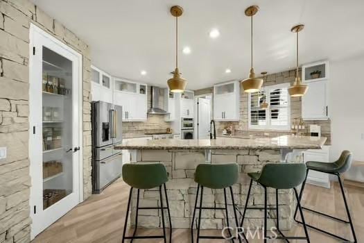 2056 Caltha Way, Perris, CA 92571 - kitchen with appliances with stainless steel finishes, wall chimney range hood, light wood-style flooring, backsplash, and white cabinetry