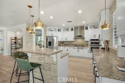 2056 Caltha Way, Perris, CA 92571 - kitchen with stainless steel appliances, wall chimney exhaust hood, tasteful backsplash, a breakfast bar area, and white cabinetry