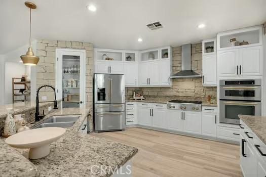 2056 Caltha Way, Perris, CA 92571 - kitchen featuring stainless steel appliances, wall chimney exhaust hood, white cabinetry, light wood-style floors, and decorative backsplash