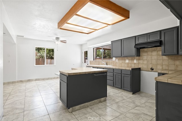 921 Christian Ave, Bakersfield, CA 93314 - kitchen with tile counters, under cabinet range hood, backsplash, a ceiling fan, and a center island