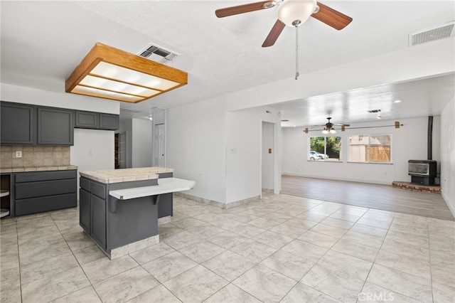 921 Christian Ave, Bakersfield, CA 93314 - kitchen featuring a ceiling fan, tile counters, tasteful backsplash, a wood stove, and open floor plan