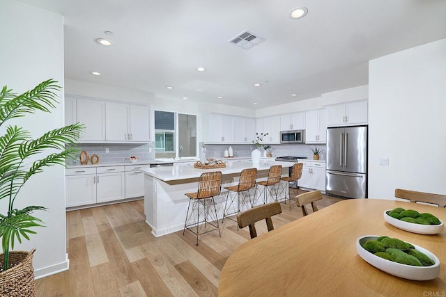 6140 Colt Pl Unit 104, Carlsbad, CA 92009 - kitchen featuring appliances with stainless steel finishes, a center island, backsplash, a breakfast bar, and light countertops