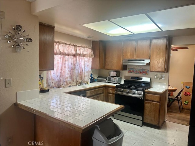 3539 Castaic, Riverside, CA 92501 - kitchen featuring stainless steel range with gas cooktop, tile countertops, under cabinet range hood, a peninsula, and brown cabinetry