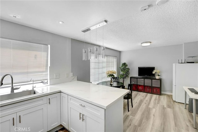 2620 W Grand Ave Unit E, Alhambra, CA 91801 - kitchen featuring decorative light fixtures, a peninsula, light wood finished floors, white cabinets, and light stone countertops