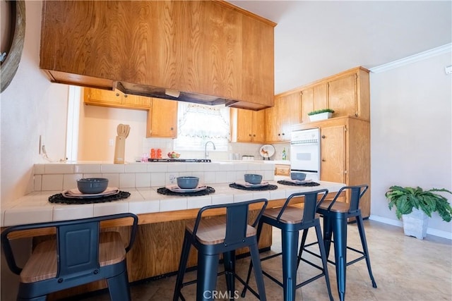 3730 E Euclid Ave, Orange, CA 92869 - kitchen with tile countertops, tasteful backsplash, a kitchen breakfast bar, ornamental molding, and a peninsula