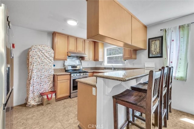 2925 Lemon St, Riverside, CA 92501 - kitchen with stainless steel range with gas stovetop, a peninsula, a kitchen breakfast bar, under cabinet range hood, and fridge