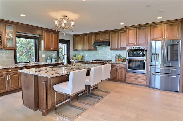 182 Denslow Ave, Los Angeles, CA 90049 - kitchen with appliances with stainless steel finishes, under cabinet range hood, backsplash, light stone counters, and recessed lighting