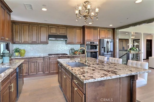 182 Denslow Ave, Los Angeles, CA 90049 - kitchen with stainless steel appliances, under cabinet range hood, a breakfast bar area, light wood-style floors, and tasteful backsplash