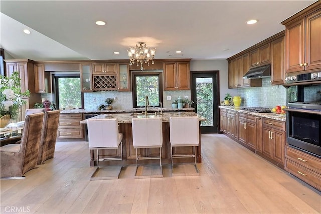 182 Denslow Ave, Los Angeles, CA 90049 - kitchen with under cabinet range hood, stainless steel appliances, tasteful backsplash, a breakfast bar, and light wood-style floors