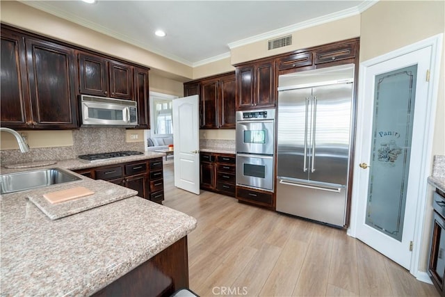 39560 Tinderbox Way, Murrieta, CA 92562 - kitchen with stainless steel appliances, light wood finished floors, dark brown cabinetry, crown molding, and light countertops