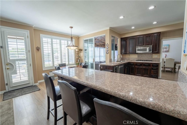 39560 Tinderbox Way, Murrieta, CA 92562 - kitchen with appliances with stainless steel finishes, ornamental molding, dark brown cabinetry, a peninsula, and a breakfast bar