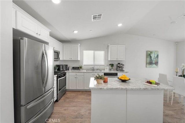 10335 Saint Andrews Ct, Adelanto, CA 92301 - kitchen featuring appliances with stainless steel finishes, white cabinets, light wood-type flooring, vaulted ceiling, and a kitchen island