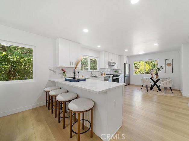 1050 Loma Verde Dr, Arcadia, CA 91006 - kitchen with light wood-type flooring, a kitchen bar, appliances with stainless steel finishes, a peninsula, and white cabinets