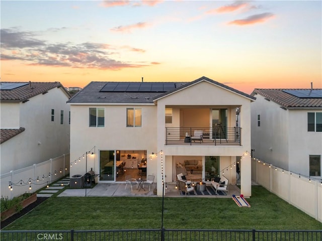28537 Daybreak Way, Saugus, CA 91350 - back of house at dusk featuring a balcony, a fenced backyard, roof mounted solar panels, and stucco siding