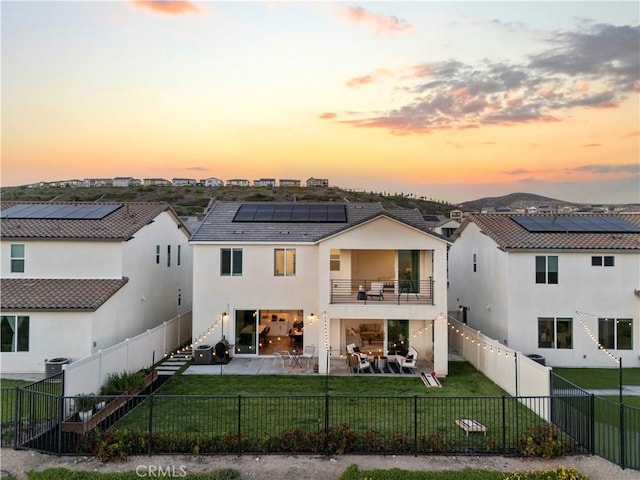 28537 Daybreak Way, Saugus, CA 91350 - back of property at dusk featuring a balcony, a fenced backyard, solar panels, a patio, and stucco siding