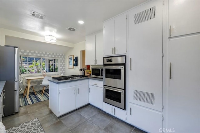 14453 Watkins Dr, La Mirada, CA 90638 - kitchen with appliances with stainless steel finishes, a peninsula, white cabinetry, light tile patterned floors, and dark countertops