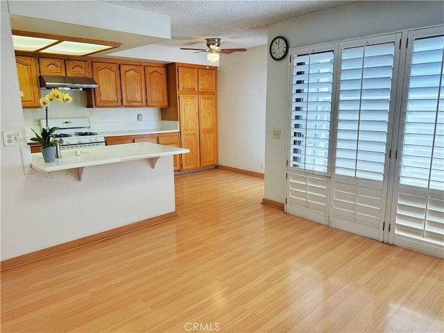 1525 Welldow Ln, Fullerton, CA 92831 - kitchen with gas range gas stove, under cabinet range hood, light countertops, a ceiling fan, and brown cabinetry