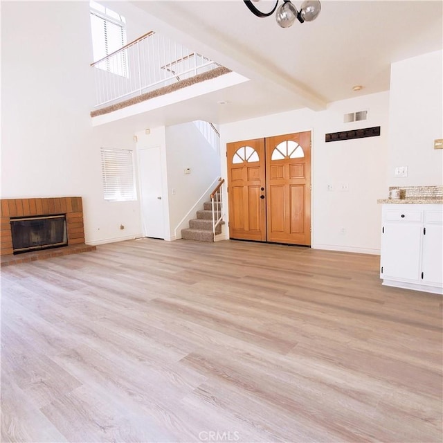 1387 Sycamore Ln, San Bernardino, CA 92408 - unfurnished living room with stairway, light wood-style floors, a fireplace, a high ceiling, and beam ceiling