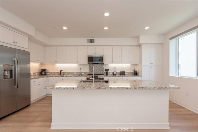 1851 S Union St Unit 10, Anaheim, CA 92805 - kitchen featuring appliances with stainless steel finishes, white cabinetry, light wood finished floors, a kitchen island with sink, and light stone counters