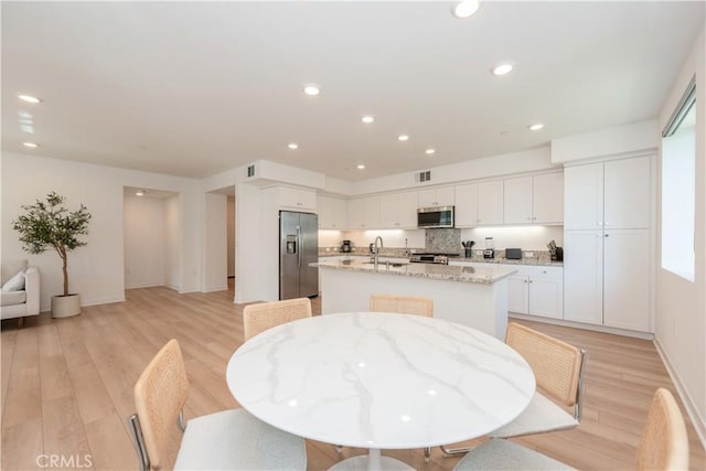 1851 S Union St Unit 10, Anaheim, CA 92805 - kitchen with appliances with stainless steel finishes, a kitchen island with sink, white cabinets, light wood-style floors, and light stone countertops