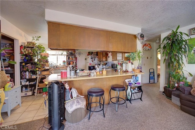 2130 Ocean St, Oceano, CA 93445 - kitchen featuring brown cabinets, a textured ceiling, a peninsula, a kitchen bar, and light countertops
